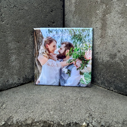 Small square magnet print of a couple embracing with flowers against a concrete wall.